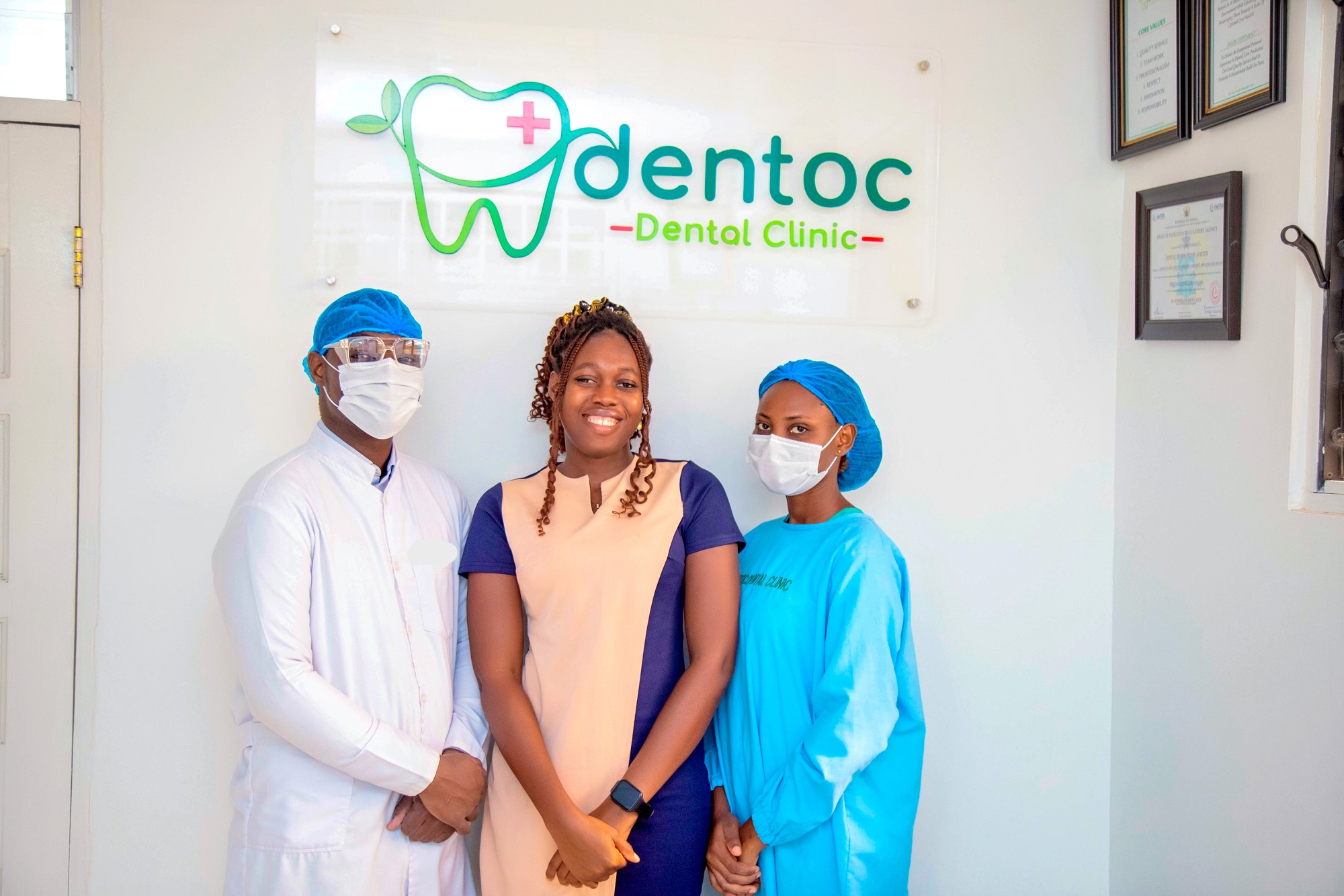 The Dentoc team standing in front of the clinic logo wall